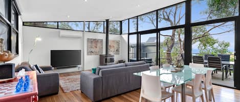 A modern living room with a large window, a flat-screen TV, a sofa, and a dining area with a glass table.