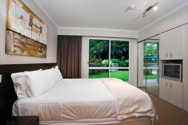 Una habitación de hotel con una cama grande, televisión y puerta corrediza a un jardín.