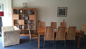 Un coin repas comprenant une table en bois et des chaises en osier, un canapé en osier et un meuble en bois doté d’étagères.