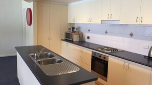 Une cuisine moderne dotée d’un îlot central, d’un évier en acier inoxydable, d’un four à micro-ondes, d’un four et d’un dosseret carrelé.