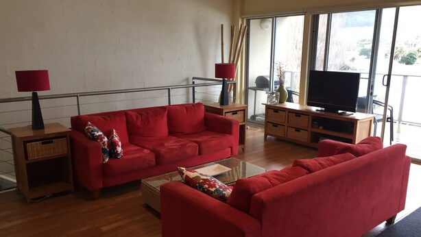 Un salon avec un canapé rouge, une table basse, un téléviseur et un balcon doté d’une rambarde.