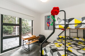 Ein Schlafsaalzimmer mit Etagenbetten, einem Schreibtisch und einem Fenster mit Blick auf einen Garten.