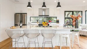 A modern kitchen with a central island, bar stools, and pendant lighting. - Allawah (Lorne)