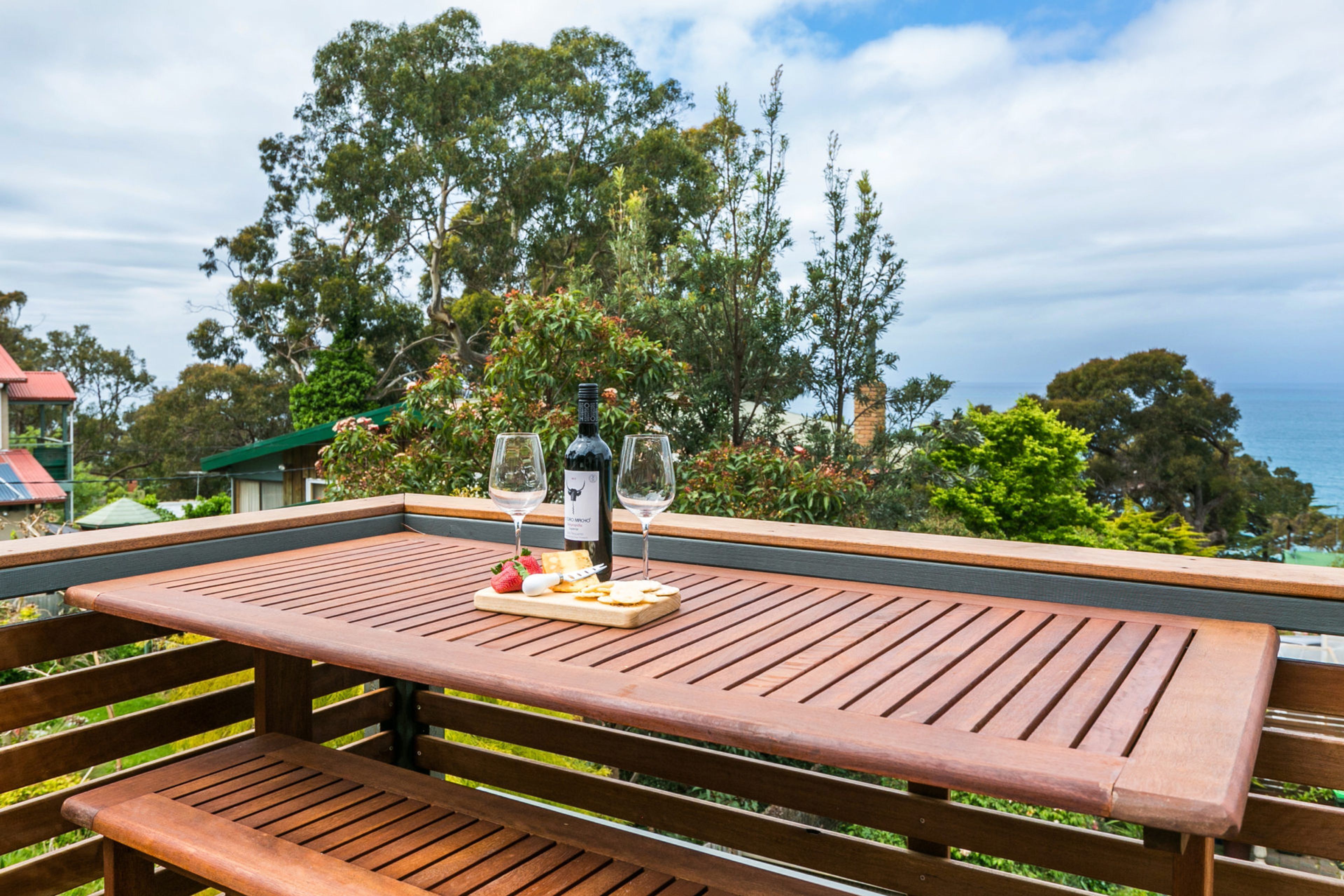 A wooden deck with a table set for a meal, overlooking a scenic view of trees and the sea.