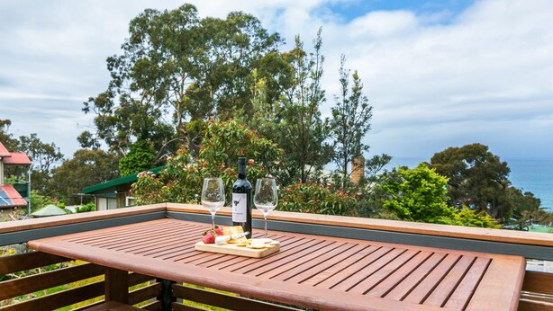 A wooden deck with a table set for a meal, overlooking a scenic view of trees and the sea. - Allawah (Lorne)