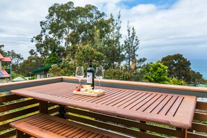 A wooden deck with a table set for a meal, overlooking a scenic view of trees and the sea. - Allawah (Lorne)