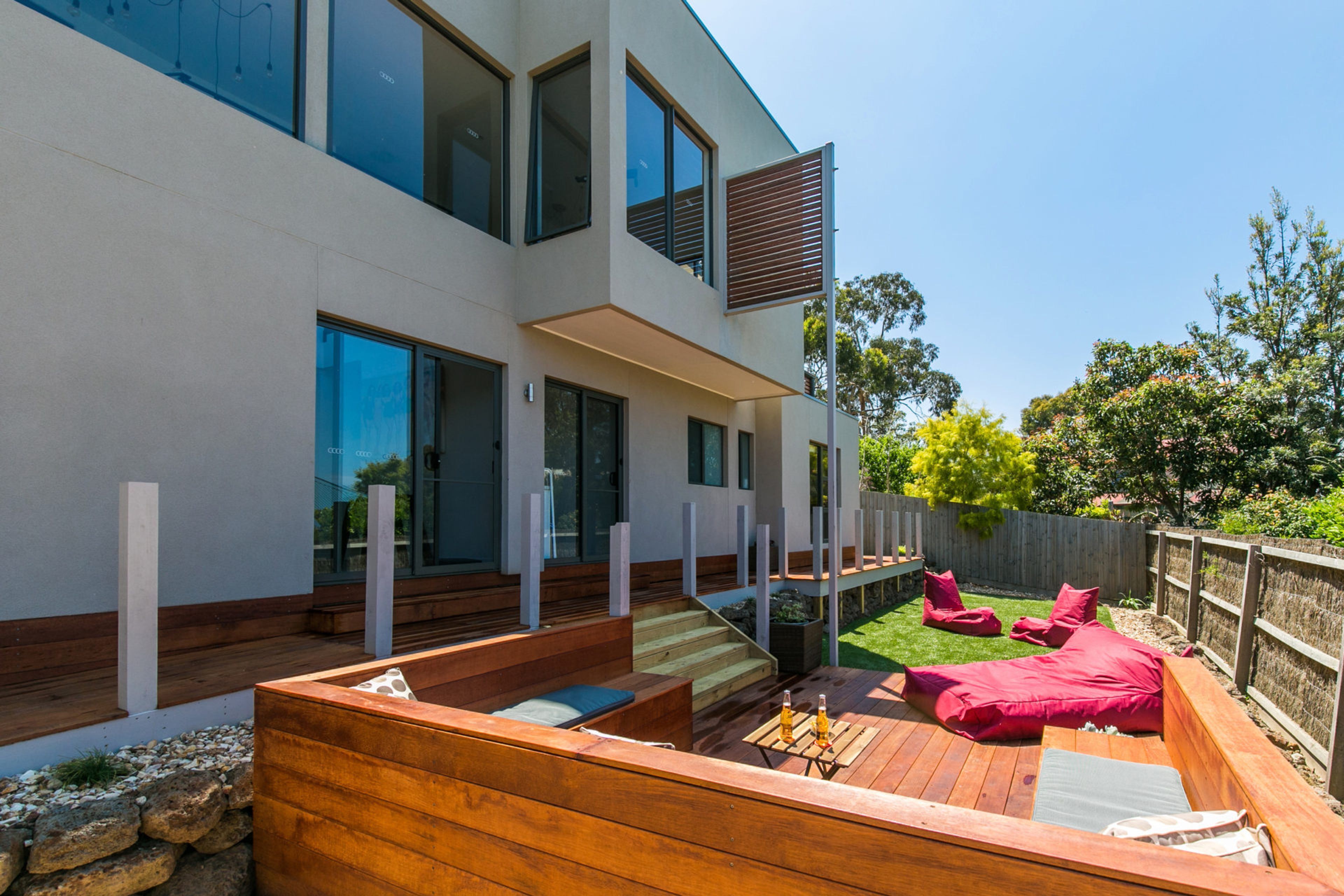 A modern house with a wooden deck, outdoor seating, and a large window.