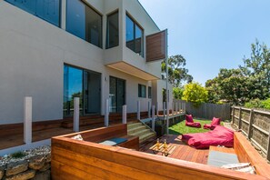 A modern house with a wooden deck, outdoor seating, and a large window. - Allawah (Lorne)