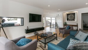 A modern living room with a flat-screen TV, a coffee table, sofas, and a staircase leading to an upper floor. - Allawah (Lorne)