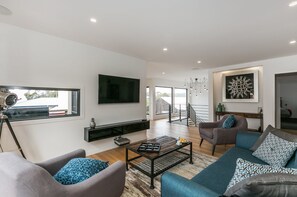 A modern living room with a flat-screen TV, a coffee table, sofas, and a staircase leading to an upper floor. - Allawah (Lorne)