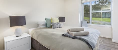 A bedroom with a bed, bedside lamps, a nightstand, a window with a view of the outdoors, and a brick-patterned wall.