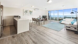 Een moderne keuken met een eethoek, een woonkamer met een bank en uitzicht op zee, en een groot raam.