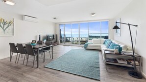A modern living room with a dining area, a large window offering a view, and a cozy seating area with a patterned rug.