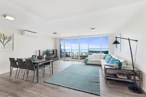 A modern living room with a dining area, a large window offering a view, and a cozy seating area with a patterned rug.