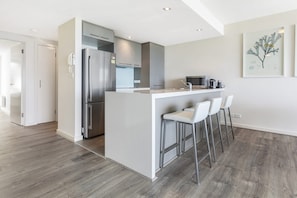 A modern kitchen with a central island, stainless steel appliances, and a bar area with stools. - Point Grey Apartment 13 (Lorne)