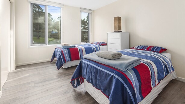 Een slaapkamer met twee bedden, een witte dressoir en grote ramen.