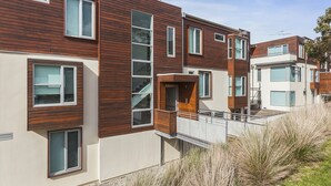 Un moderno edificio residenziale a più piani con pannelli esterni in legno e bianco, ampie finestre e una scala visibile che porta a un balcone.