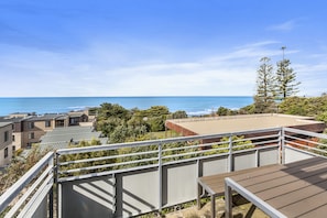 A rooftop terrace with a view of the ocean, surrounded by greenery and modern buildings. - Point Grey Apartment 13 (Lorne)