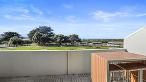 Ein Balkon mit Blick auf eine Wiese, Bäume und ein entferntes Gewässer.