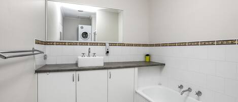 A bathroom with a white sink, a mirror, a bathtub, and a towel rack.