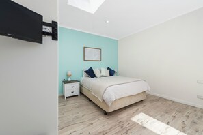 Ein Schlafzimmer mit Bett, Nachttisch, Lampe und einem an der Wand befestigten Fernseher.