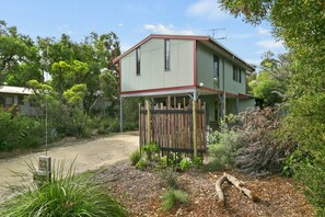 A two-story house with a fenced front yard, surrounded by trees and vegetation.