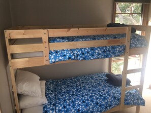 Ein Etagenbett mit Bettzeug in blauem Sternenmuster und ein Fenster mit Blick auf Bäume.