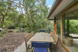 An outdoor wooden deck with a table and benches, surrounded by lush greenery and trees.