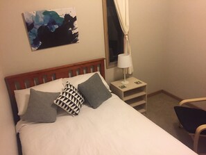 A bed with pillows, a bedside table with a lamp, and a painting on the wall.