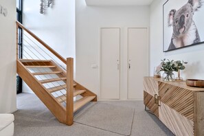 A modern interior with a wooden staircase, a white door, and a wooden cabinet with a vase. - Skenes Beach House Ocean Views set in Natural Bush (Skenes Creek, Apollo Bay)
