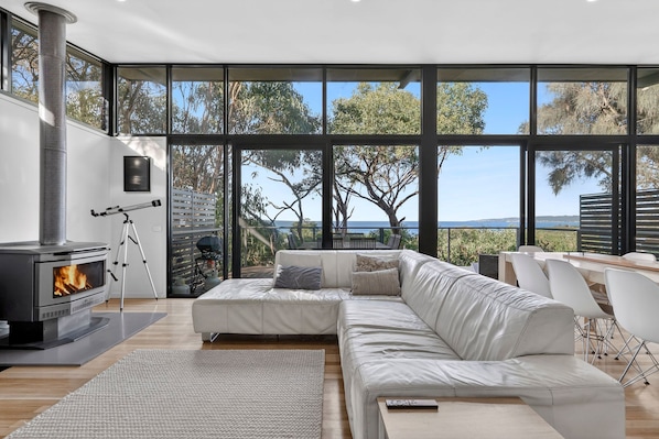 A modern living room with a large window, a fireplace, a sofa, and a telescope.