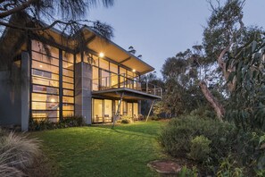 A modern house with a large glass facade, a balcony, and a well-maintained lawn.