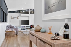 A modern living room with a sofa, a television, a bookshelf, and a wooden table with decorative items. - Skenes Beach House Ocean Views set in Natural Bush (Skenes Creek, Apollo Bay)