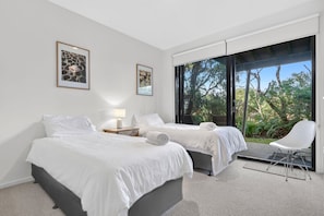 A hotel room with two beds, a sitting area, and a large window with a view of trees. - Skenes Beach House Ocean Views set in Natural Bush (Skenes Creek, Apollo Bay)