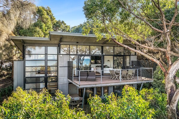 A modern house with a deck, large windows, and a view of the surrounding greenery.