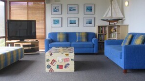 A living room with a blue sofa set, a television, a bookshelf, and framed pictures on the wall.