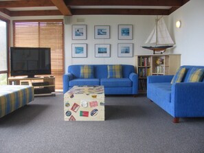 A living room with a blue sofa, a television, a bookshelf, and a sailboat model. - Ocean View - Views Galore (Separation Creek)