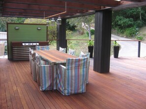 An outdoor deck with a wooden table and striped chairs, a grill, and hanging lanterns.