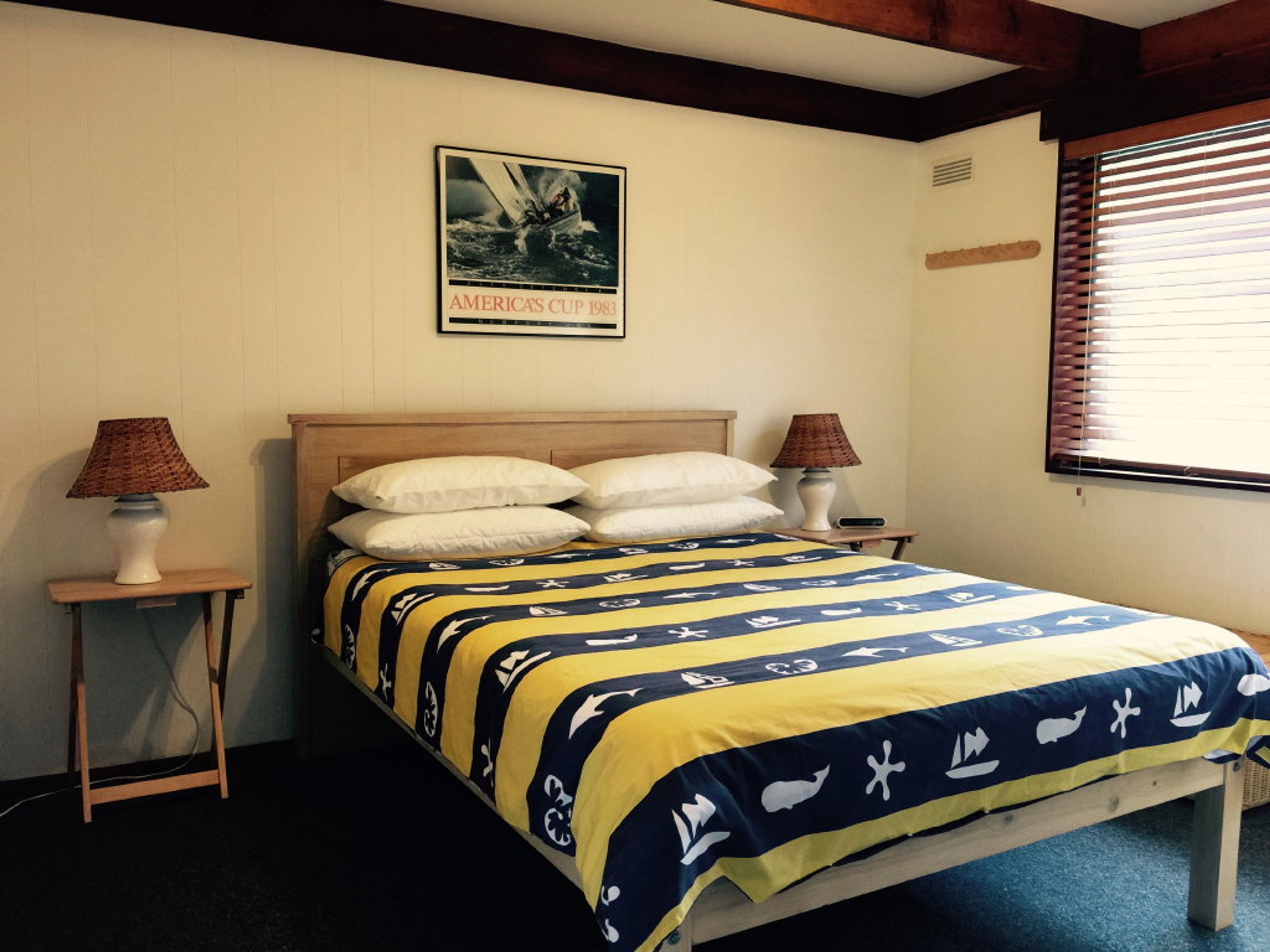 Ein Schlafzimmer mit einem Bett, zwei Nachttischlampen, einem Bild an der Wand und einem Fenster mit Jalousien.