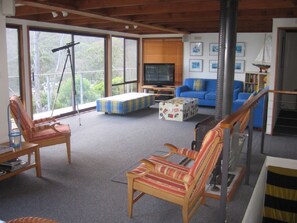 A spacious living room with a large window, a television, a blue sofa, and striped chairs.