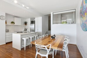 Une cuisine moderne avec des meubles blancs, une table à manger en bois et des chaises blanches.