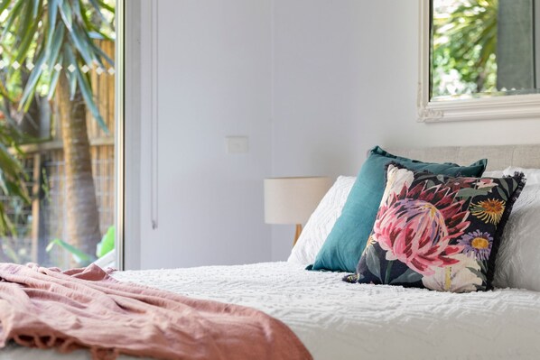 Une chambre à coucher avec un lit, des oreillers, une couverture, une fenêtre et une porte.