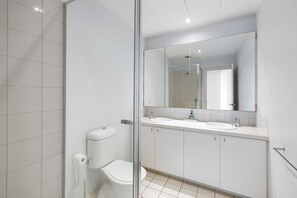 A modern bathroom with a glass shower enclosure, a toilet, and a double sink vanity. - Apartment 18 Kalimna (Lorne)