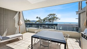 Ein Balkon mit Tisch, Stühlen, einer Couch und Blick auf das Meer und Bäume.