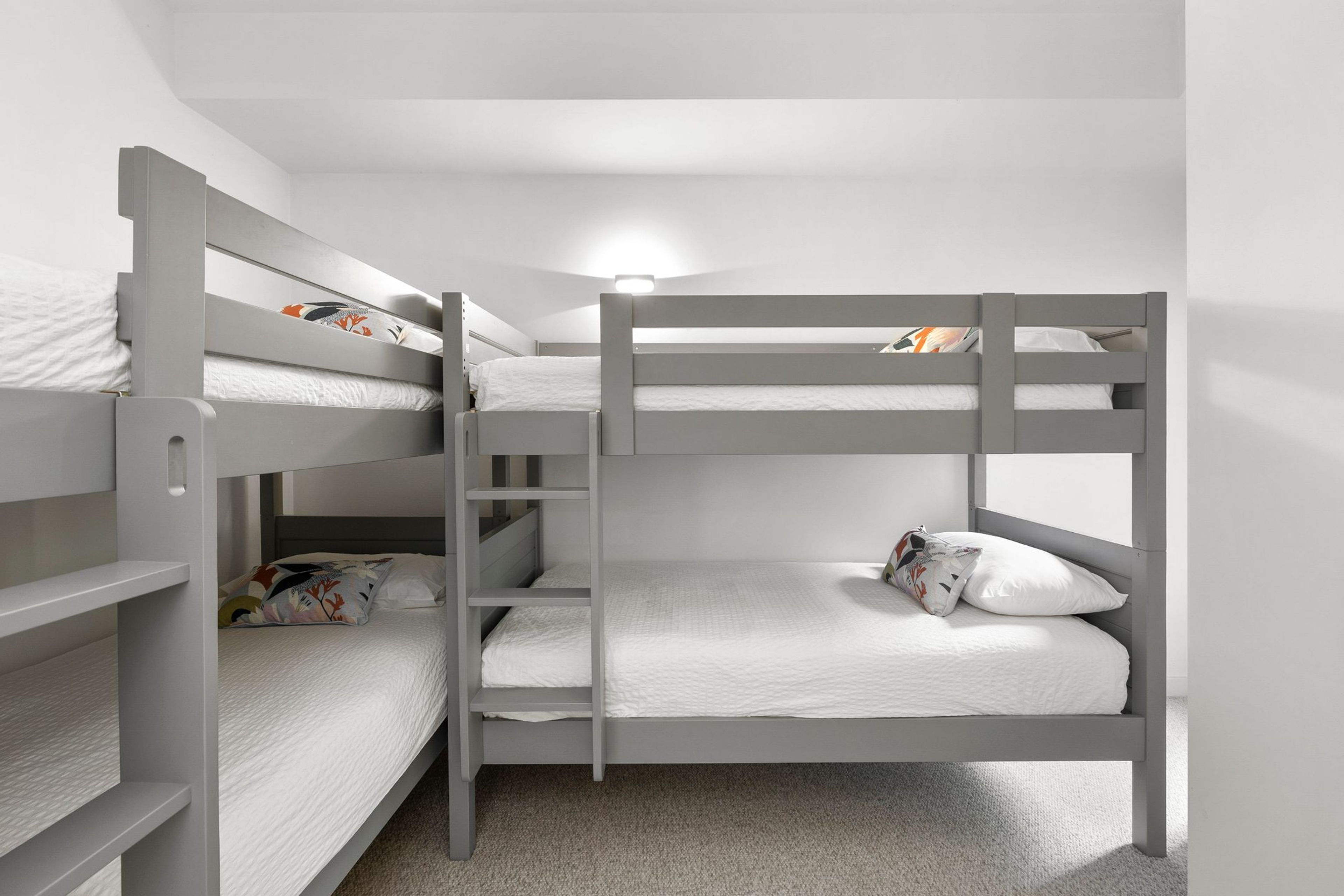 A bunk bed room with a ladder, white bedding, and a light fixture above the beds.