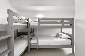 Une chambre avec un lit superposé, une échelle, du linge de lit blanc et un luminaire au-dessus des lits.
