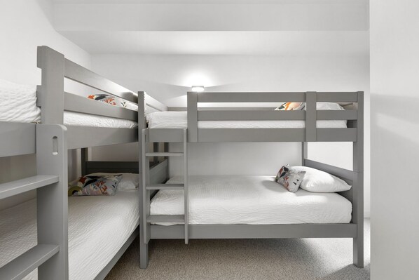 Habitació amb lliteres i una escala, roba de llit blanca i un llum penjant sobre els llits.