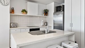 Eine moderne Küche mit weißen Schränken, einem Edelstahlkühlschrank, einem eingebauten Backofen und einem Spülbecken mit Armatur aus Edelstahl.