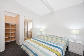 Een slaapkamer met een bed, nachtkastjes, een kledingkast en een badkamer zichtbaar door een geopende deur.