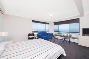 Een hotelkamer met een bed, een bureau, een stoel en een televisie. Grote ramen bieden uitzicht op de oceaan.